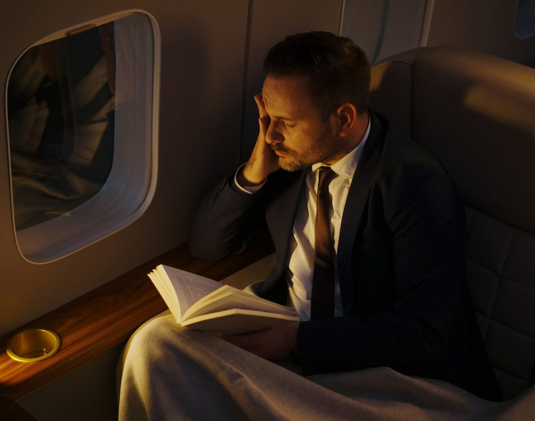 Exhausted businessman holding a book and resting his head on his hand while traveling in a private jet, dealing with stress and fatigue during a luxurious business trip